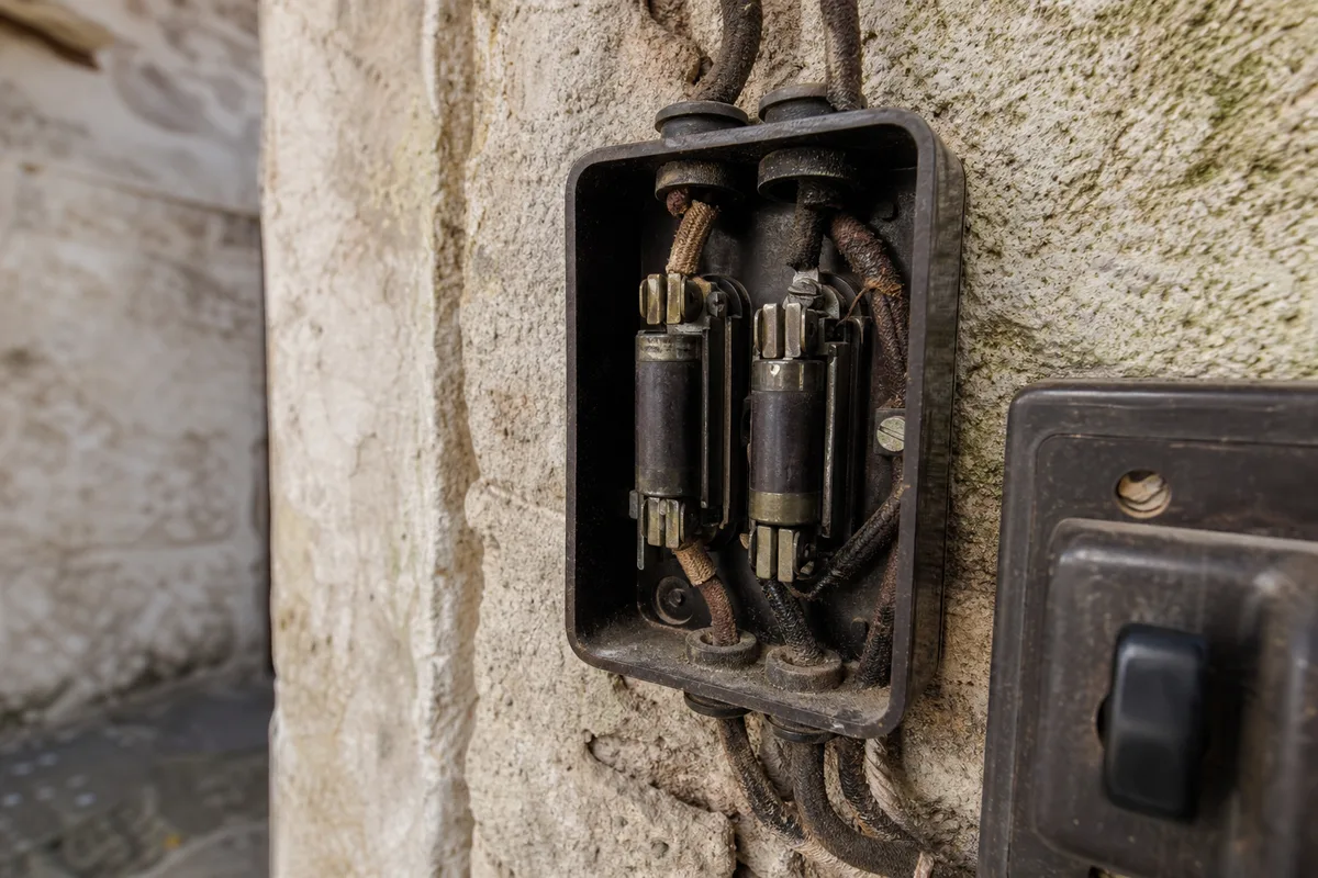 Tableau électrique ancien à fusibles dans une maison de bord de mer, câblage vétuste apparent