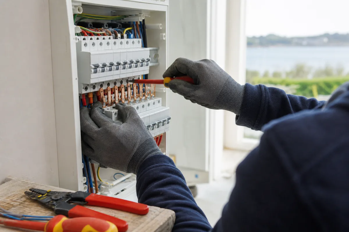 Coffret électrique neuf en cours de raccordement, mains d&rsquo;un artisan, lumière claire d&rsquo;atelier